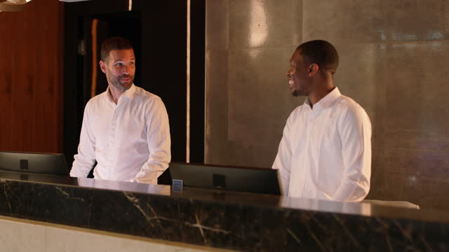 Two interracial hotel receptionists talking while working together