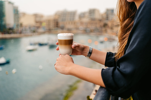 Beautiful young woman drinking coffee in a café on the terrace in Saint Julian's bay in Malta. Close-up.