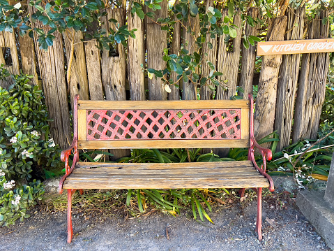 Horizontal landscape photo of a decorative wood and painted metal bench seat in a country garden near Ulladulla, south coast NSW in a sunny day in Winter.