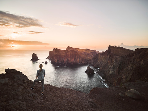 Back view of a female athlete looking at view on coastline of Ponta De Sao Lourenco at sunset. Copy space.