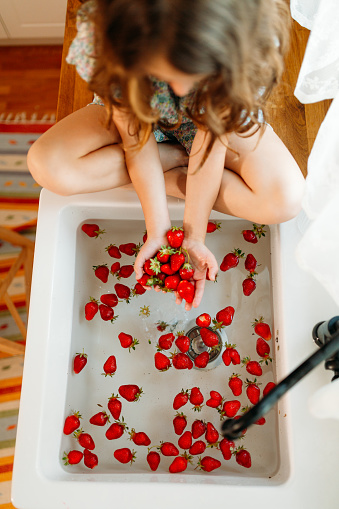 Girl washing and tasting fresh picked strawberries from the garden