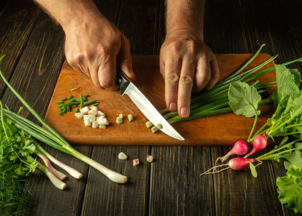 The cook cuts the onion with a knife on the kitchen cutting board. Vegetarian products or fresh vegetables on the kitchen table for a healthy breakfast