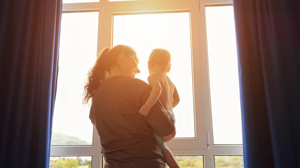 istock Mother with toddler in arms opens curtains on window 1505369542