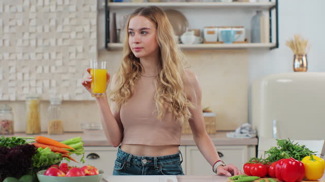 Woman drinking an orange juice at kitchen. Attractive sporty girl drinking freshly juice. Lifestyle and healthy nutrition concept.