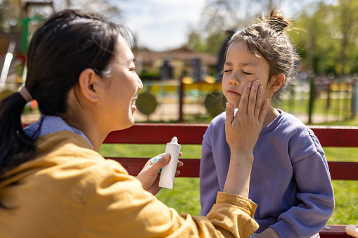 Mid adult Japanese woman applying sun-screen to her daughters face