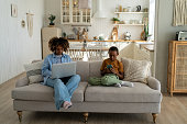 African American mother and son looking into phone and laptop. Mom busy, child with phone