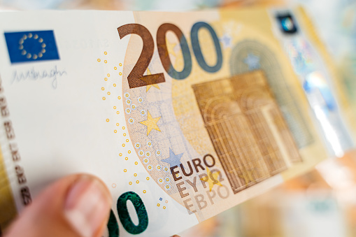 Male hand holding a single two hundred Euro above heap of assorted colorful EURO bills laid down on a flat surface.