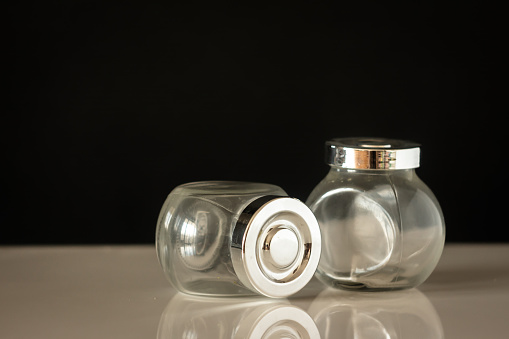 two glass jars - storage containers - with shiny lids on a white table with a dark background