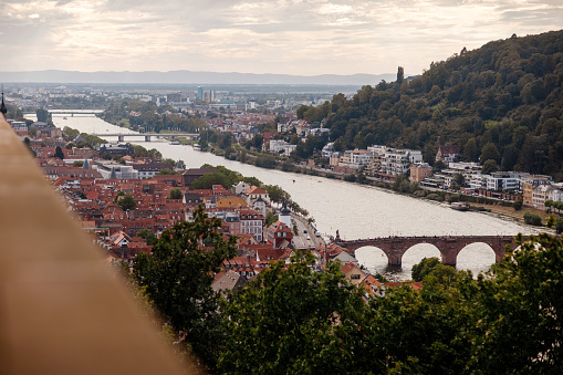Aerial drone view over famous city of Heidelberg Germany with bridge on river Neckar. Dramatic cloudy sky with sunbeams over old town and mountains.