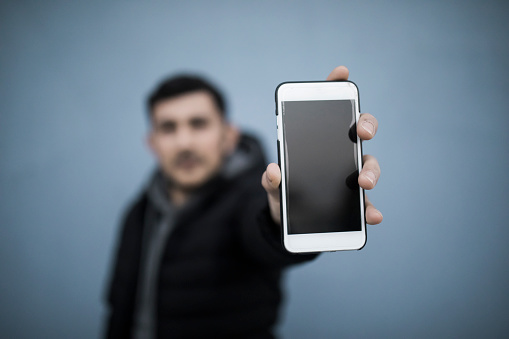 Portrait of real syrian man showing smartphone on blue background selective focus