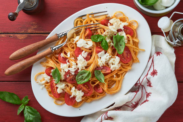 istock Salad caprese or pasta spaghetti broken with basil and mozzarella ala caprese on a white plate on red rustic wooden background. Traditional Italian cuisine. Italian food concept. Top view. 1505495473