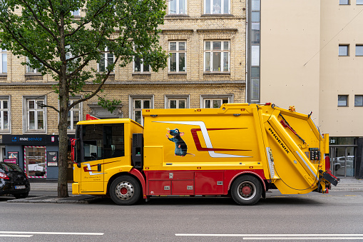 Copenhagen, Denmark - June 30, 2023: A large yellow and red trash truck in the streets of Copenhagen.