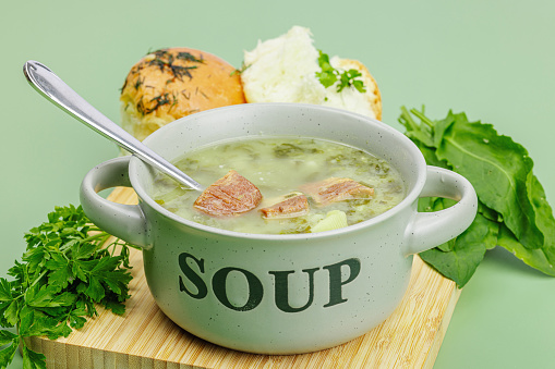 Traditional Portuguese soup Caldo Verde with fresh bakery. Aromatic greens, served dish, ready for eat healthy food. Modern wooden stand, green background, close up