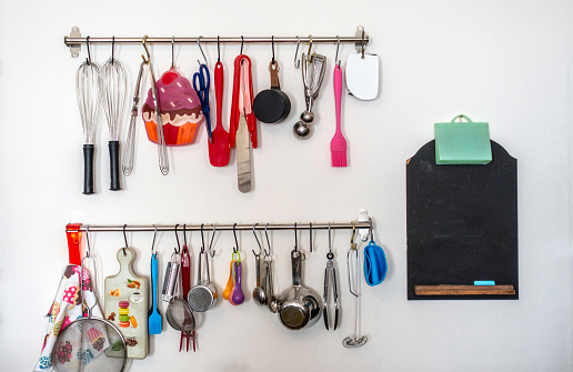 Metal rail with kitchen tools, kitchen utensils hanging, apron and seasoning in front of a white wall in the kitchen