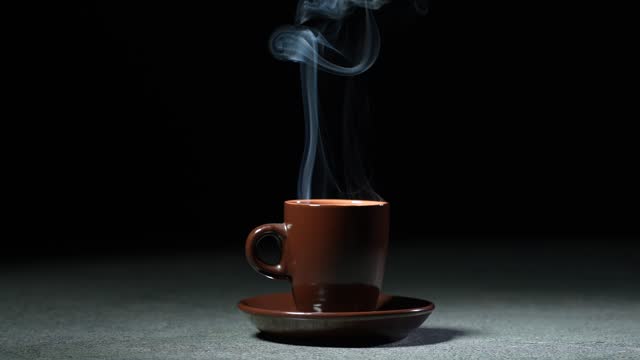 Cup with hot coffee on the table on a black background. Slow motion