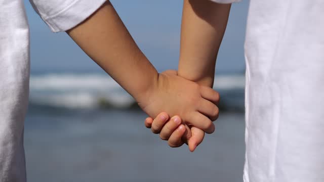 Emotionally calm, soothing shots of children's hands on shore of sea. Two small children holding hands, standing on seashore. Close up of tanned hands of children 6-10 years old who hold hands.