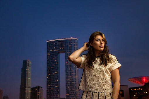 Pensive middle-aged adult lady businesswoman at Dubai skyscraper night city, bored looking away. Confident jewish woman in summer vacation, resting lady. Leisure activity concept. Copy ad text space