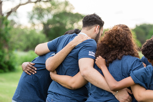 While volunteering at the park, the diverse group embraces one another.