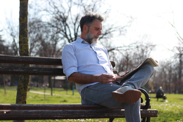 istock Mature man sitting on bench read newspaper 1505566498
