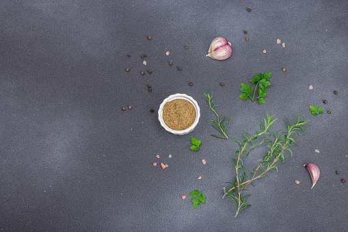 Culinary background with spices and fresh herbs. Garlic, rosemary, sea salt, black peppercorn. Black stone concrete background, flat lay, top view