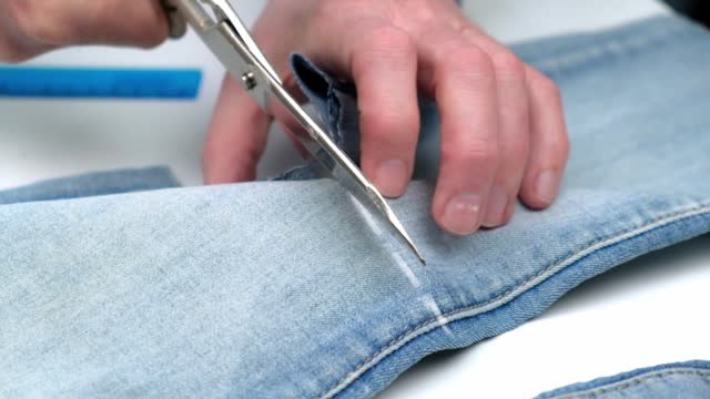 tailor cuts the leg of jeans with scissors for shortening and making summer shorts. slow motion.