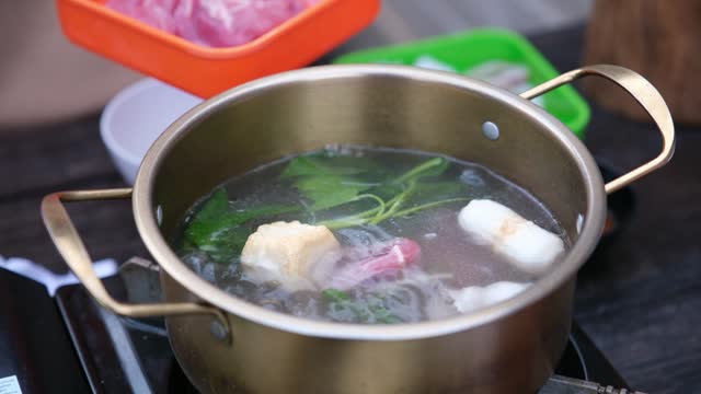 People preparing food and putting a piece of pork into a hot pot