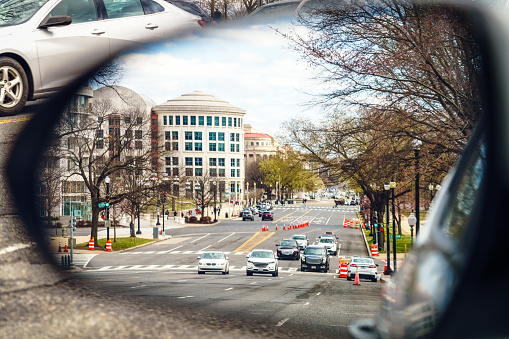 A driver's view of oncoming traffic approaching from behind, as seen in the side mirror of a car in downtown Washington DC.