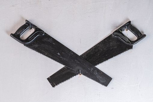 Two crossed black hand saw on a white stucco wall, close up