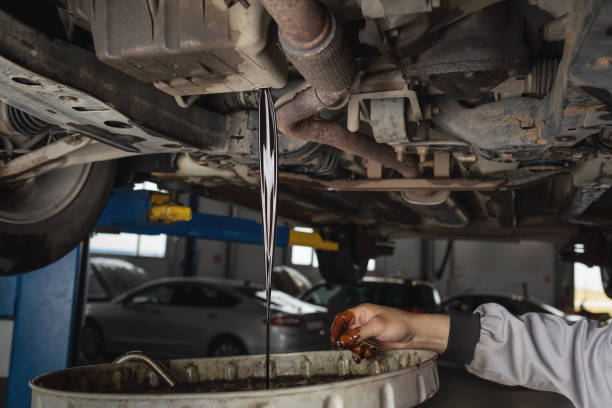 Auto mechanic drains old used engine oil at a service station, scheduled service maintenance of a passenger car stock photo