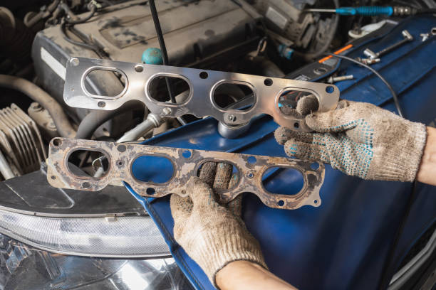 Auto mechanic holding old and new manifold gaskets for passenger car engine in front of him, post-warranty service at technical inspection station stock photo