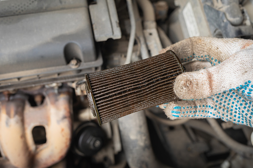 Auto mechanic holds in his hand an old oil filter to be replaced, post-warranty service in a car service