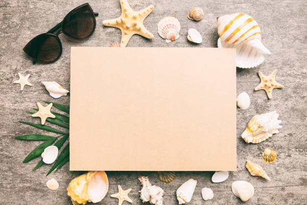 istock Summer time concept with blank greeting card and blank craft paper on colored background. Seashells from ocean shore in the shape of frame separated with space for text top view 1505641646
