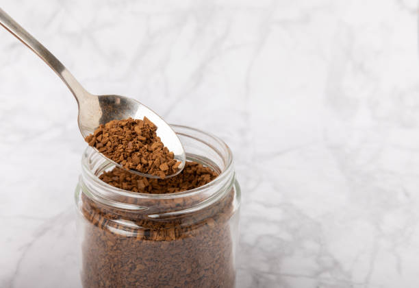 istock Instant coffee in a spoon and a glass jar on a  marble background. Place for text. Space for copy text 1505642289