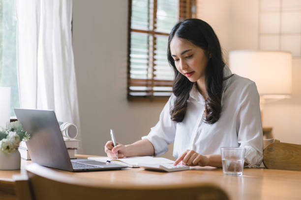 istock Young Asian female working with financial papers at home, using a calculator to count before paying taxes and receipts online. The millennial woman planning budget for saving money. 1505658339