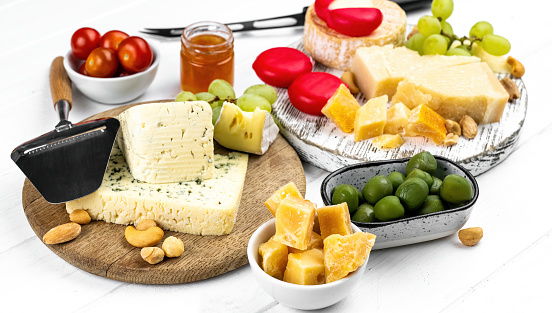 Different kinds of cheese served with green olives, tomato and grape for gourmet nutrition. Organic parmesan and brie with honey delicatessen