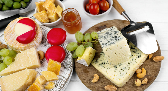 Different kinds of cheese served with green olives, tomato and grape for gourmet nutrition. Organic parmesan and brie with honey delicatessen