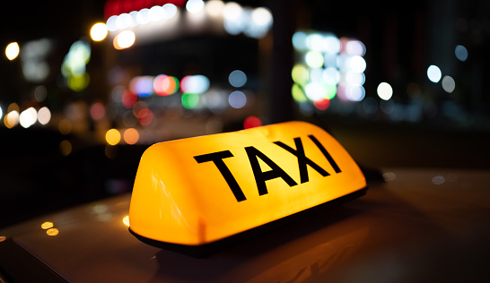 Taxi car light on dark street at night closeup. Cab sign on the vehicle transportation roof illuminates in the dusk