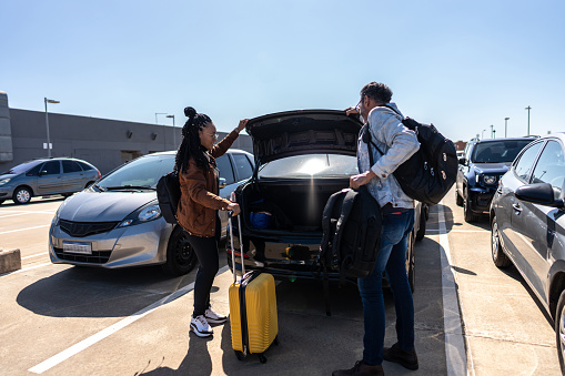 Friends picking luggage from the car trunk in parking lot at the airport