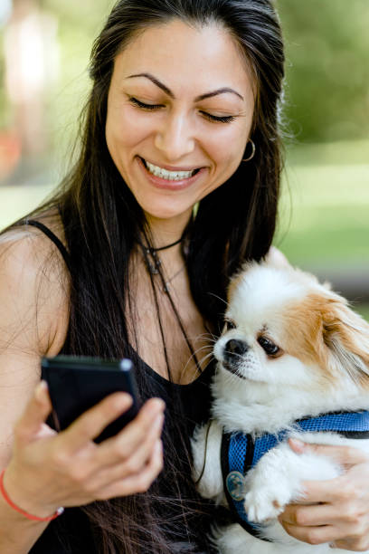 istock Young woman using phone while walking her small dog in the park 1505719183
