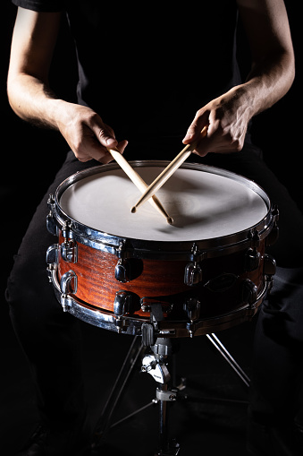 man plays musical percussion instrument with sticks closeup on a black background, a musical concept with the working drum, beautiful lighting on the stage. High quality photo
