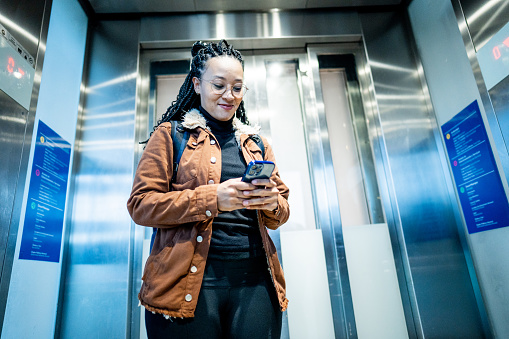 Young woman using mobile phone inside of elevator at the airport