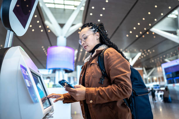 istock Young woman using self service check-in machine while use phone at the airport 1505727603