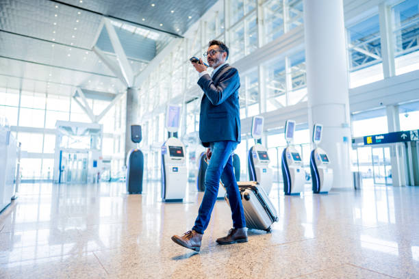 businessman walking and sending audio message using mobile phone at the airport - vocoder imagens e fotografias de stock