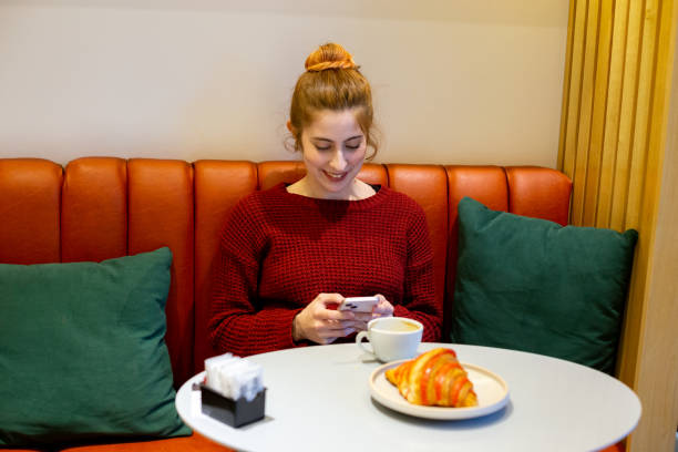 mujer joven escribiendo en el teléfono móvil en una cafetería - croissant telephone coffee shop on the phone fotografías e imágenes de stock