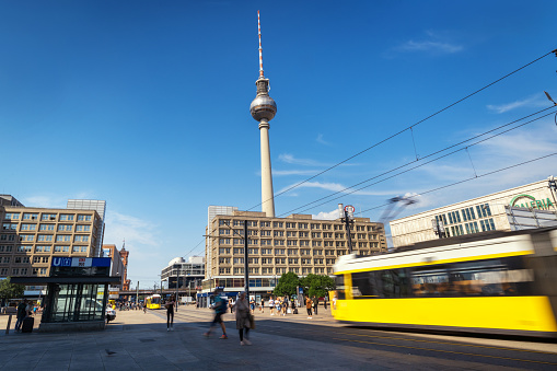 Motion-blurred yellow trams converge on Berlin's Alexanderplatz, bustling with passengers, architecture, and vibrant city energy.\n\nBerlin, Germany