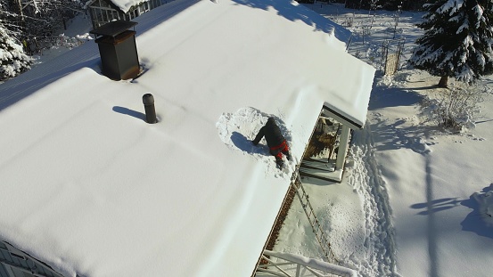 Drone shot above a home owner cleaning and shoveling snow a solar panels on a house roof