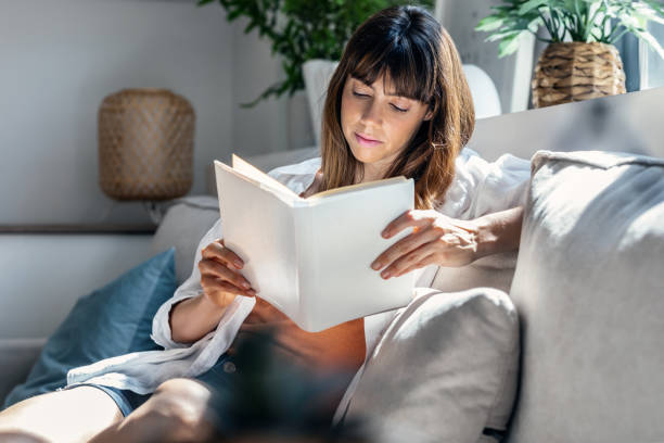 istock Pretty young woman reading a book while sitting on sofa at home. 1505823312