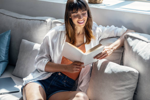istock Pretty young woman reading a book while sitting on sofa at home. 1505823315