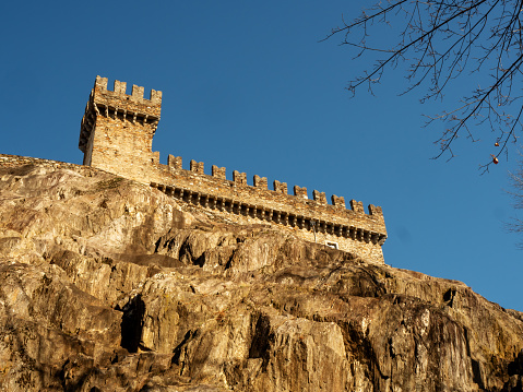 Bellinzona, Switzerland,02-28-2020: View from below the medieval castle of Bellinzona, Switzerland, set on a steep cliff, with its typical battlements, under a clear blue sky