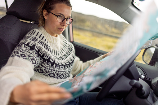 A female tourist sitting in the driver's seat and looking at a city map